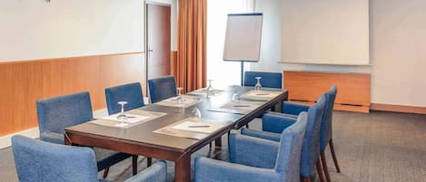 A conference room with a long table, six blue chairs, a projector screen, and a whiteboard.
