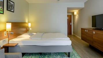 Ein Hotelzimmer mit einem Bett, Nachttischlampen, einem Fernseher, einem Holzschrank und einem gemusterten Teppich.