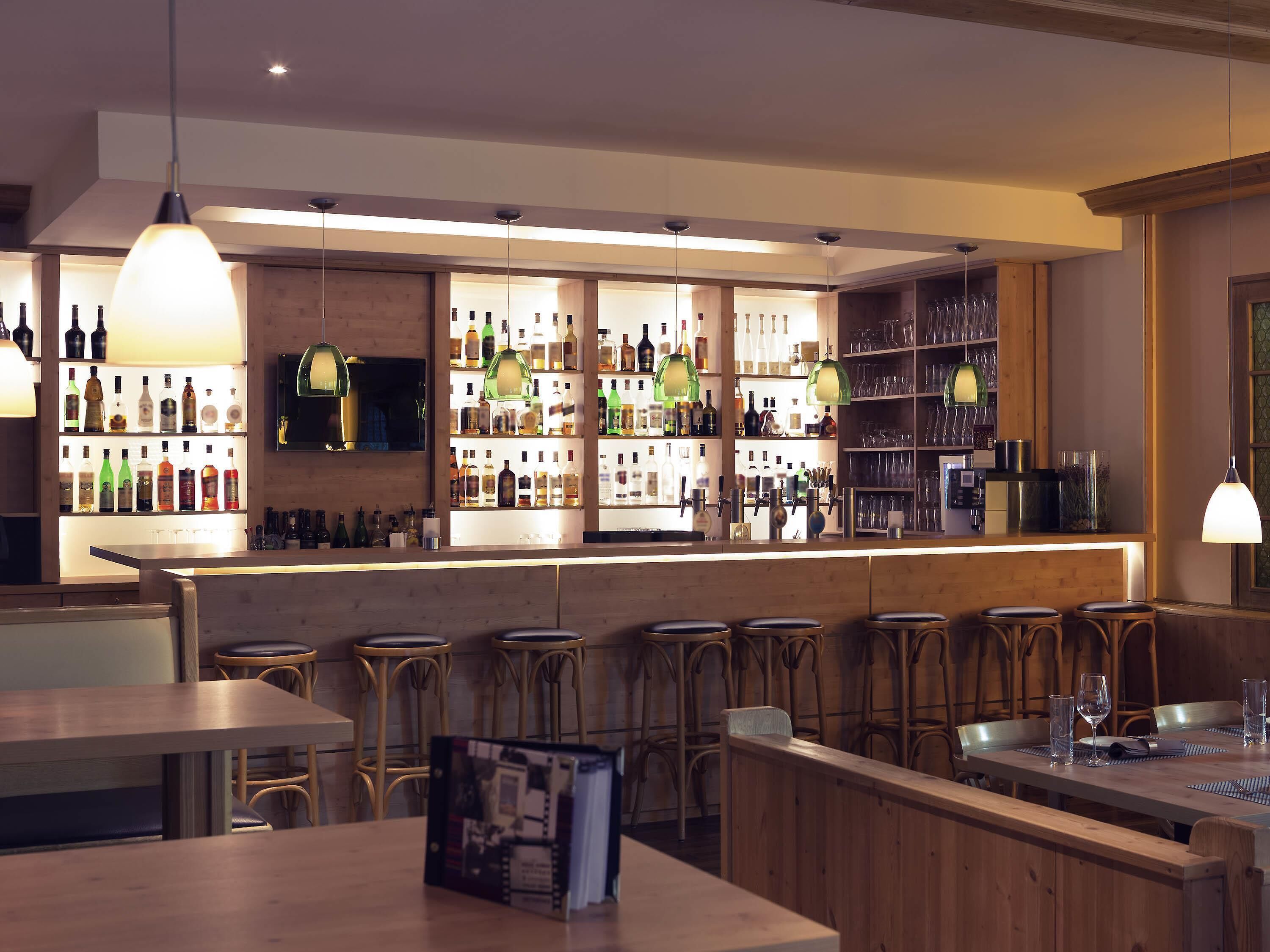 Una zona de bar con mostradores de madera, taburetes y estantes llenos de botellas y vasos.