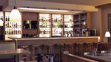 Una zona de bar con mostradores de madera, taburetes y estantes llenos de botellas y vasos.