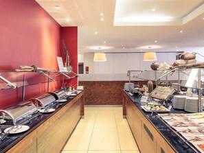 Enjoy a delicious breakfast at our hotel's central breakfast area, featuring a coffee machine and a selection of pastries and fresh fruits.