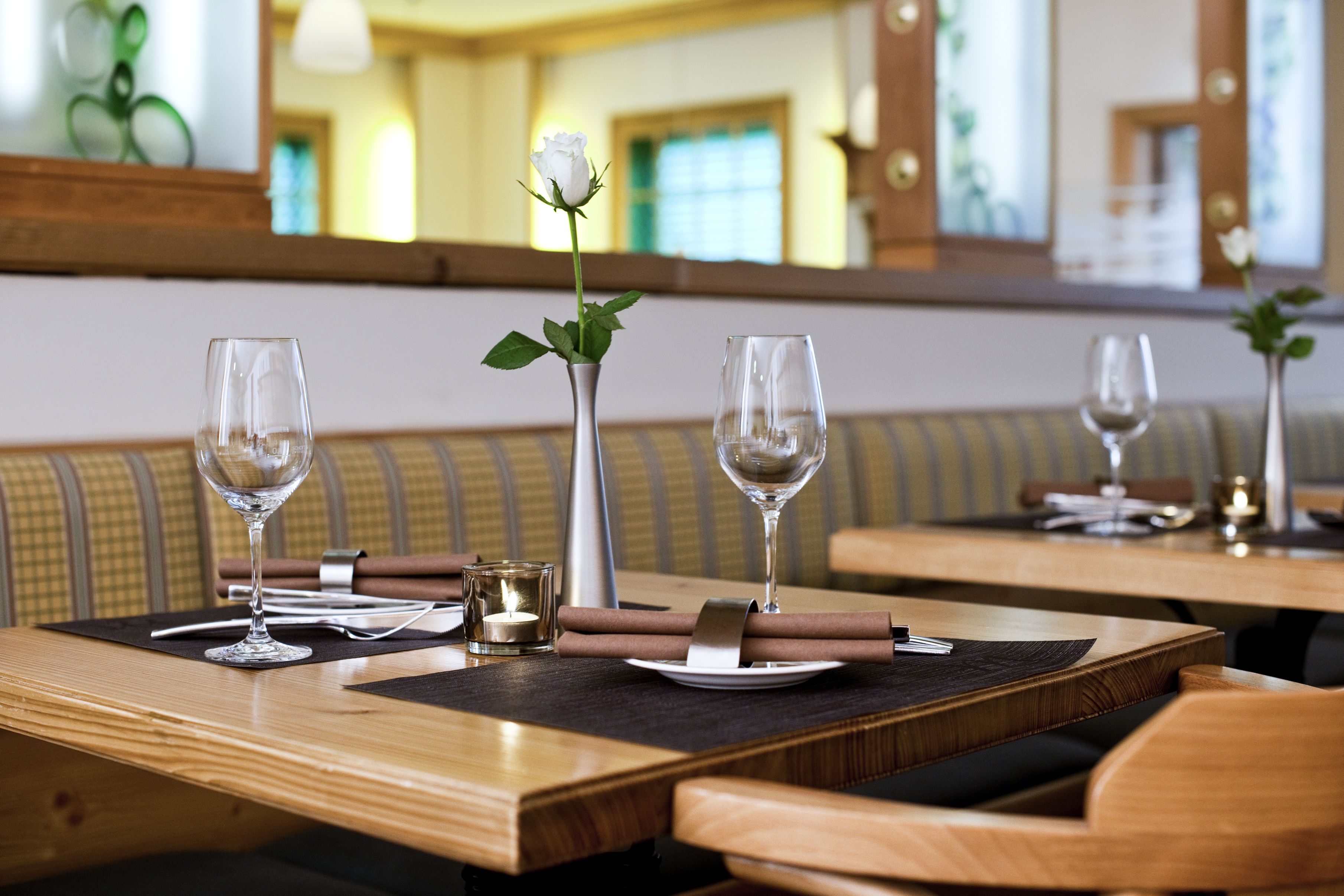 A dining table with two wine glasses, a vase with a single white rose, and a candle.