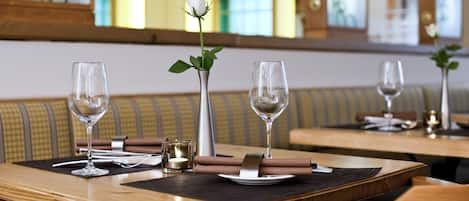 A dining table with two wine glasses, a vase with a single white rose, and a candle.