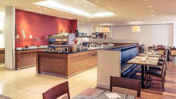 A modern restaurant with a central counter, seating area, and a red accent wall.