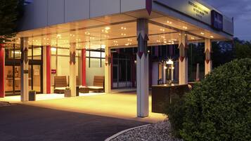 Entrada d'un hotel modern amb una zona d'estar exterior coberta, una recepció i un cel serè.