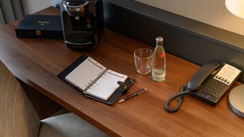 Ein Holztisch mit Notizbuch, Stift, Kaffeemaschine, Wasserflasche, Glas und Telefon.