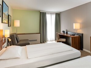 Two beds with crisp linens, a desk, and a seating area await guests in this stylish room.