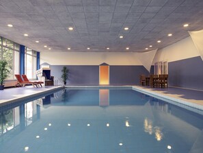 An indoor swimming pool with clear blue water, surrounded by lounge chairs, a small table, and potted plants. - Mercure Hotel Stuttgart Sindelfingen an der Messe (Sindelfingen)