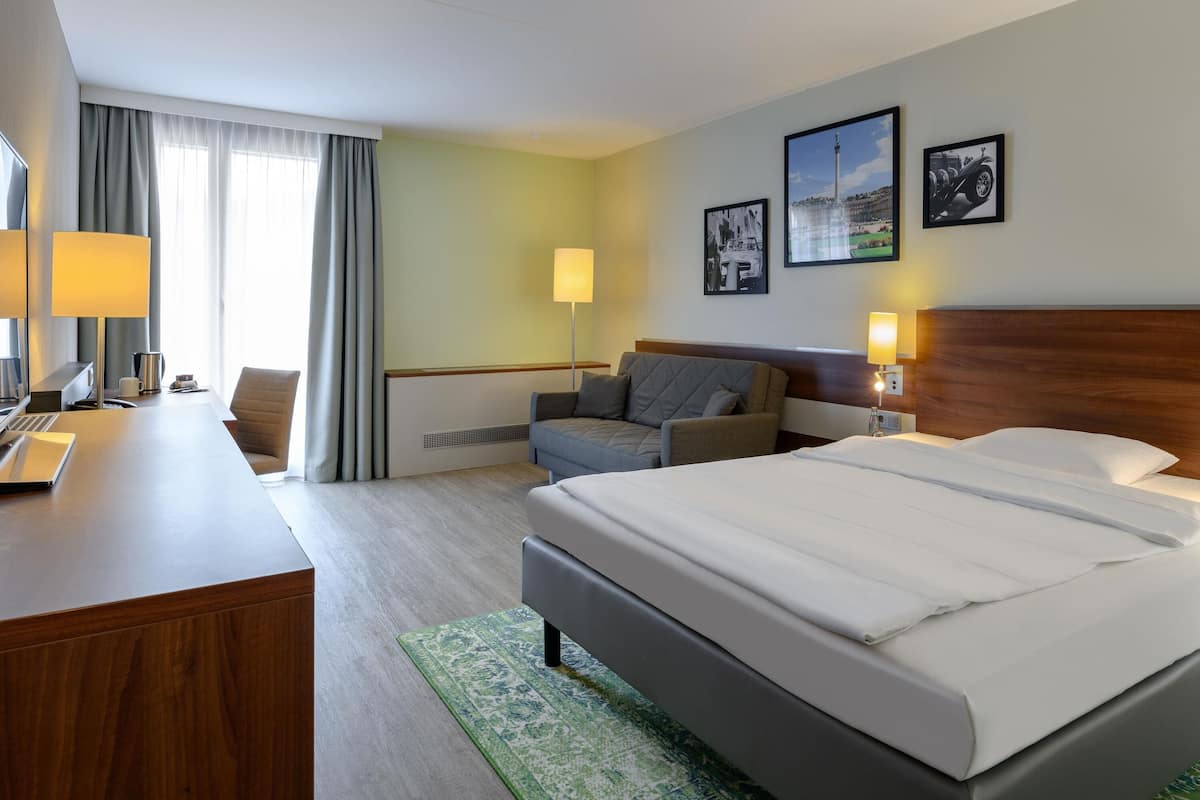 A hotel room with a bed, a desk, a chair, a sofa, and two wall-mounted lamps.