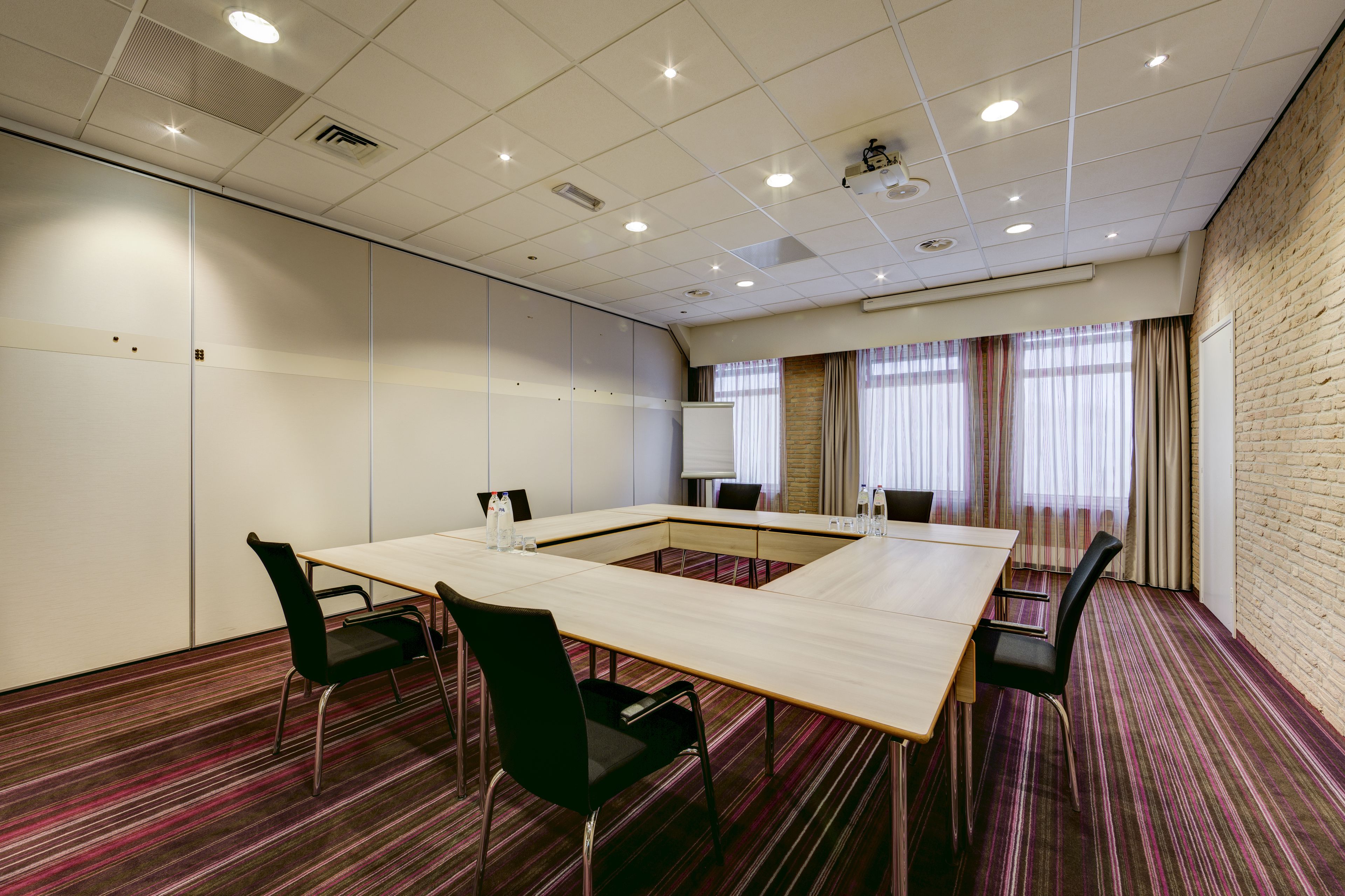 A conference room with a large rectangular table, four chairs, and a brick wall.