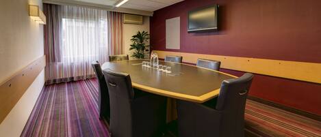 A conference room with a large table, chairs, a TV on the wall, and a striped carpet.