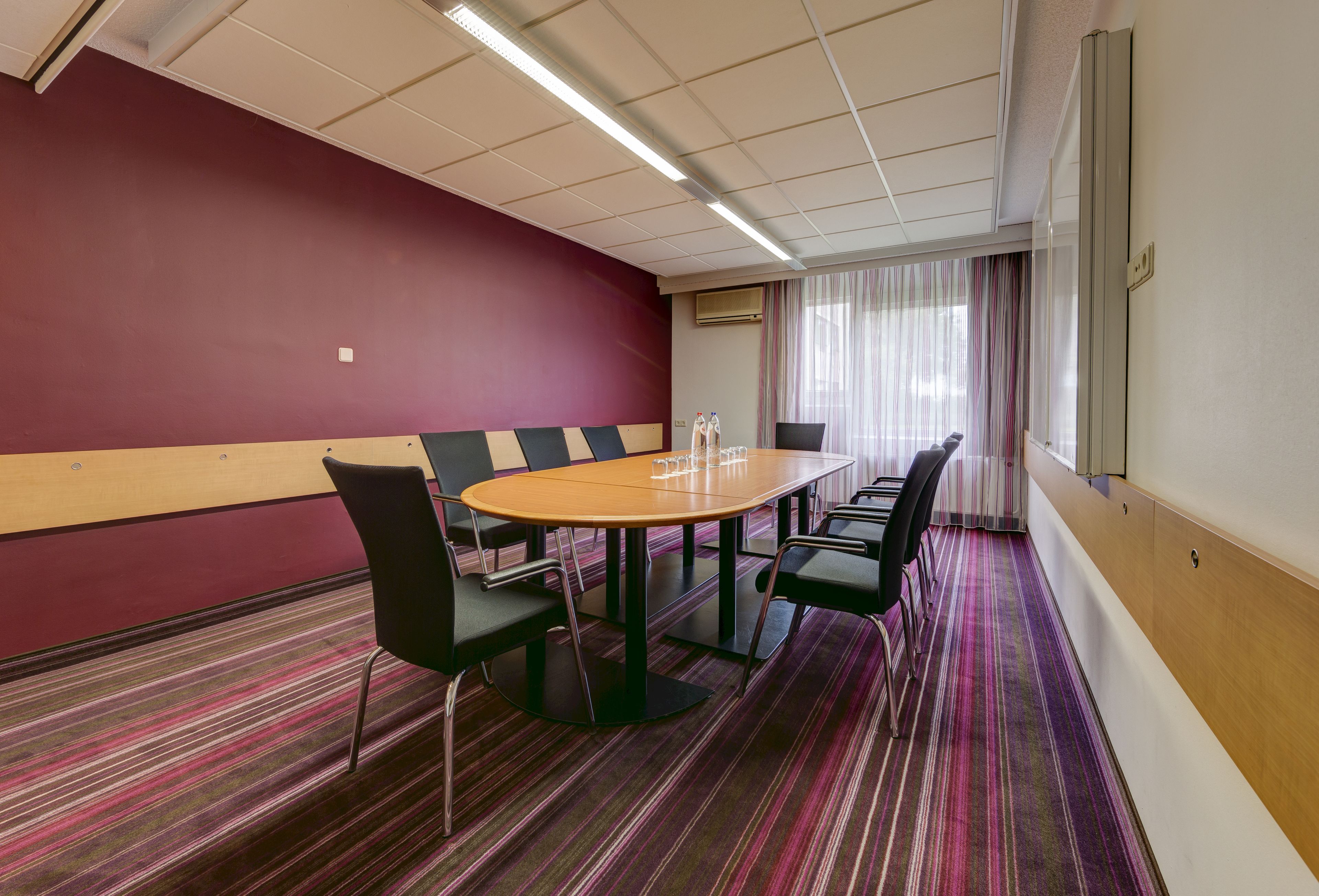 A conference room with a round table, chairs, and a carpeted floor.