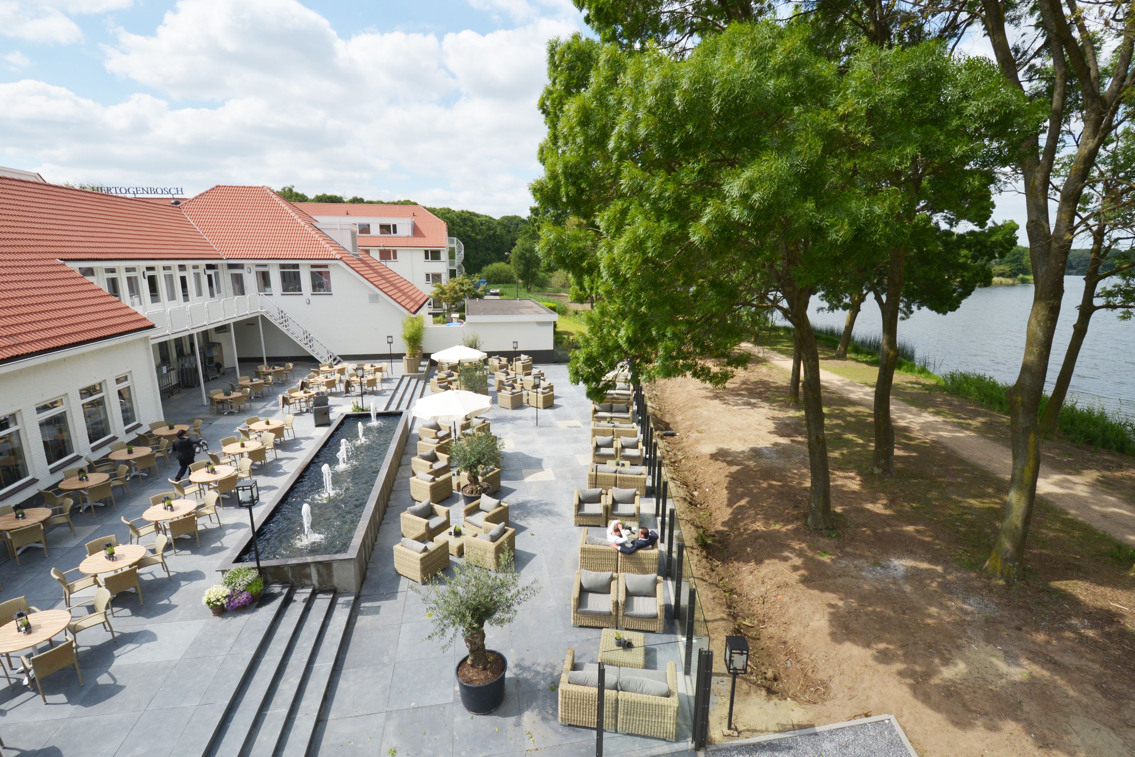 Un patio de hotel con mobiliario exterior, una fuente de agua y vistas a un lago.