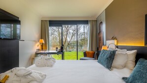 A hotel room with a large bed, a desk with a lamp, a TV, and a view of the outdoors. - Postillion Hotel Deventer (Deventer)