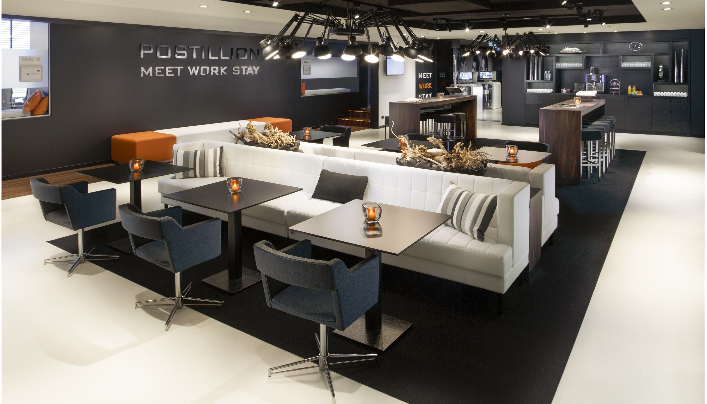 A modern lounge area with seating arrangements, a coffee station, and a wall with motivational text.