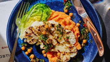 Een bord eten met gegrilde bloemkool, kikkererwten en een salade.
