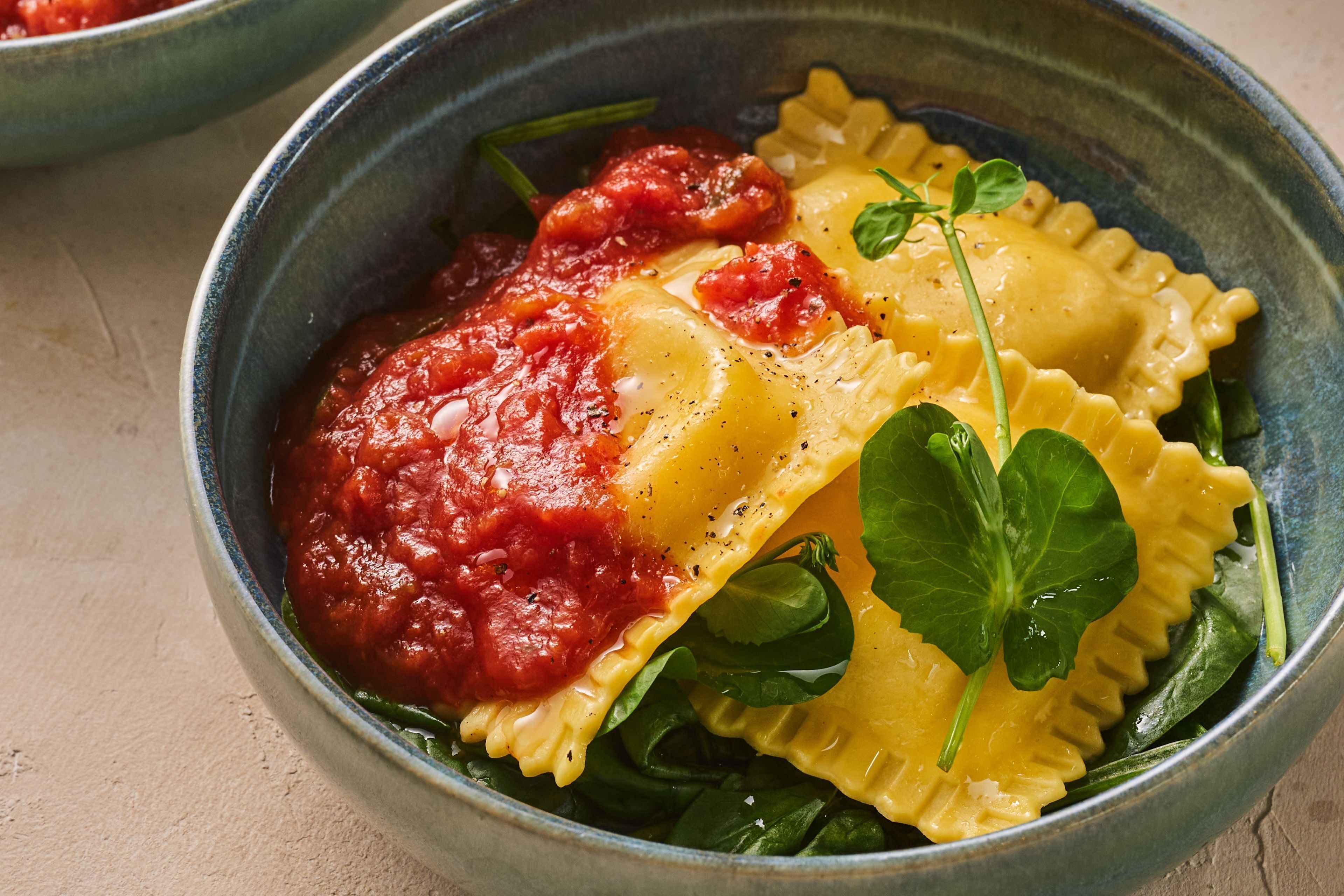 A bowl of ravioli with tomato sauce and spinach.
