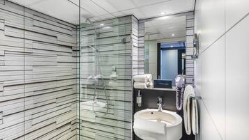 A modern bathroom with a glass shower enclosure, a sink with a mirror, and a telephone.