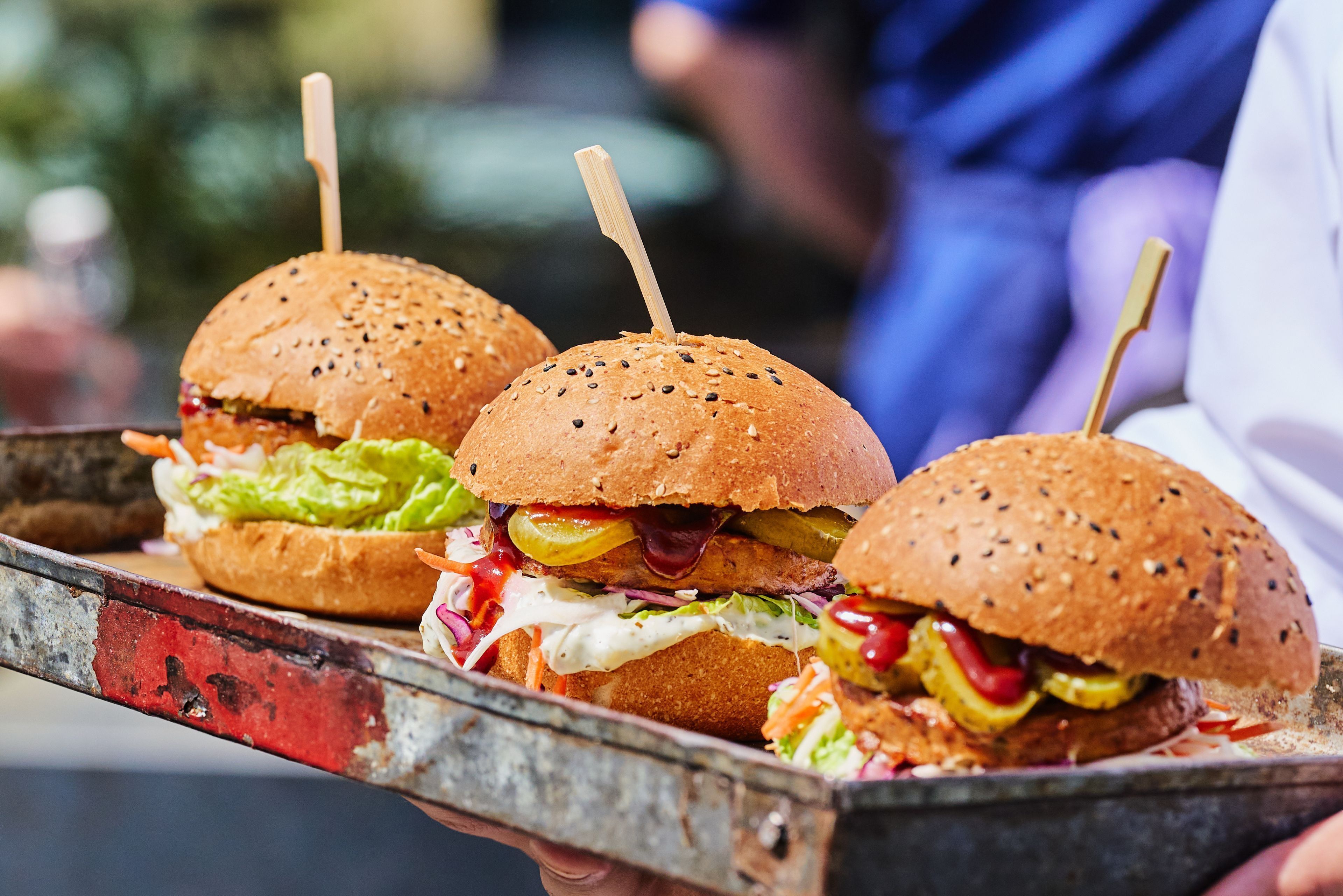 A tray with three burgers, each with a toothpick, on a metal tray.