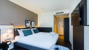 A hotel room with a large bed, a desk with a lamp, a chair, and a suitcase.