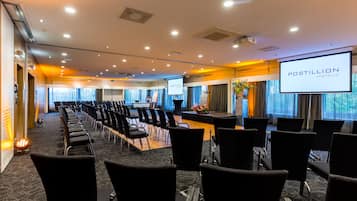 Un salón de conferencias con filas de sillas, un escenario y una gran pantalla que muestra 'POSTILLION HOTELS'.