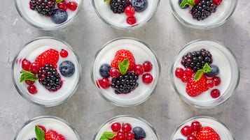 Seis tazones de yogur coronados con diversas bayas y hojas de menta.