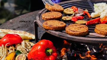A grill with grilled meat patties, vegetables, and a red bell pepper.