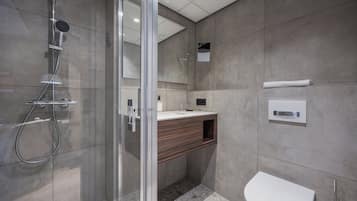 Een moderne badkamer met een douchecabine van glas, een houten wastafelmeubel en een wit toilet.