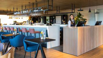 Un bar moderno con barra de madera, sillas azules y un barista detrás de la barra.