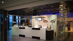 A modern reception desk with glass partitions, a digital screen, and a decorative vase display. - Postillion Hotel Utrecht Bunnik (Bunnik)