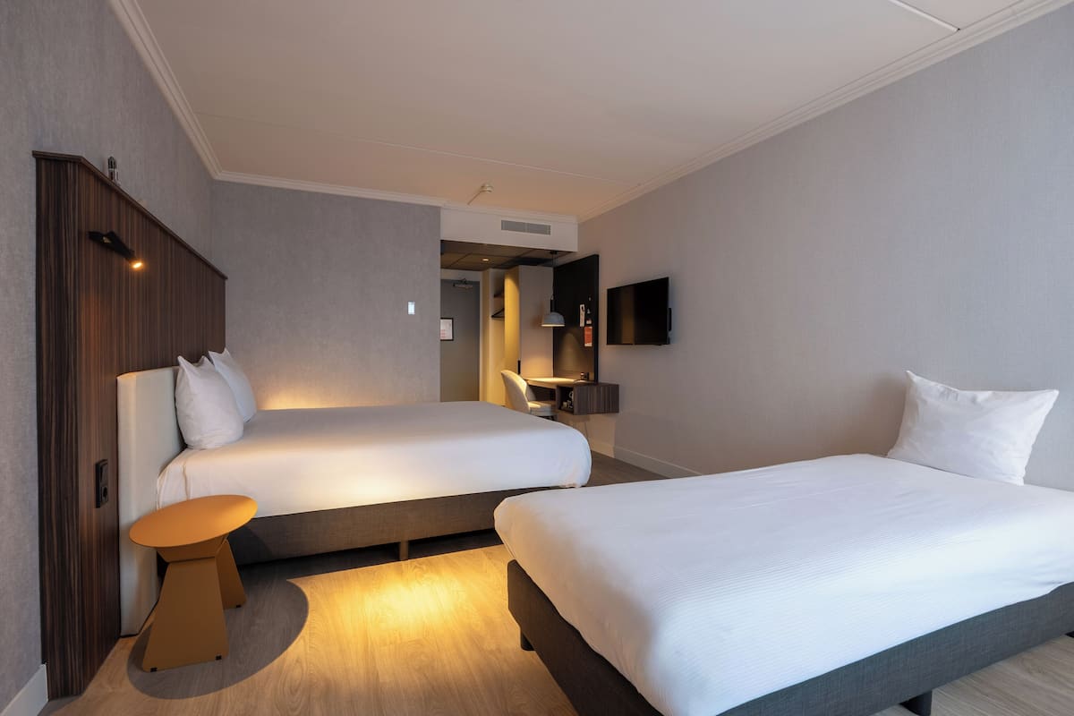A hotel room with two beds, a desk, a chair, and a TV mounted on the wall.
