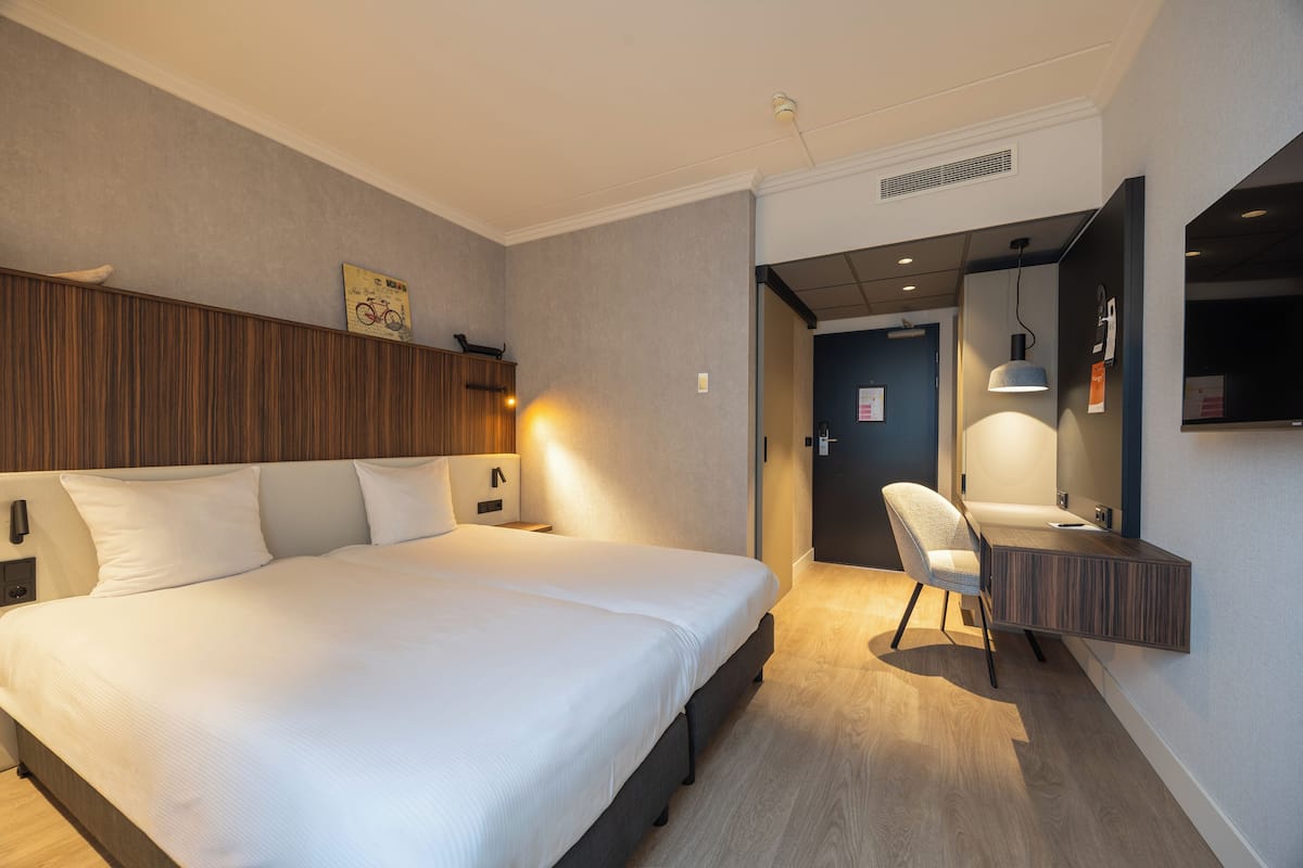 A modern hotel room with a large bed, a desk with a mirror, and a chair.