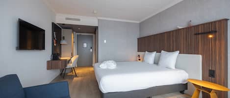 A modern hotel room with a large bed, a desk, a chair, and a sofa.