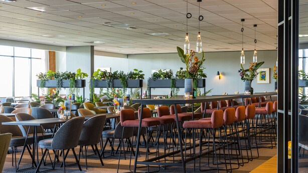A modern dining area with multiple tables and chairs, indoor plants, and pendant lighting. - Postillion Hotel Utrecht Bunnik (Bunnik)
