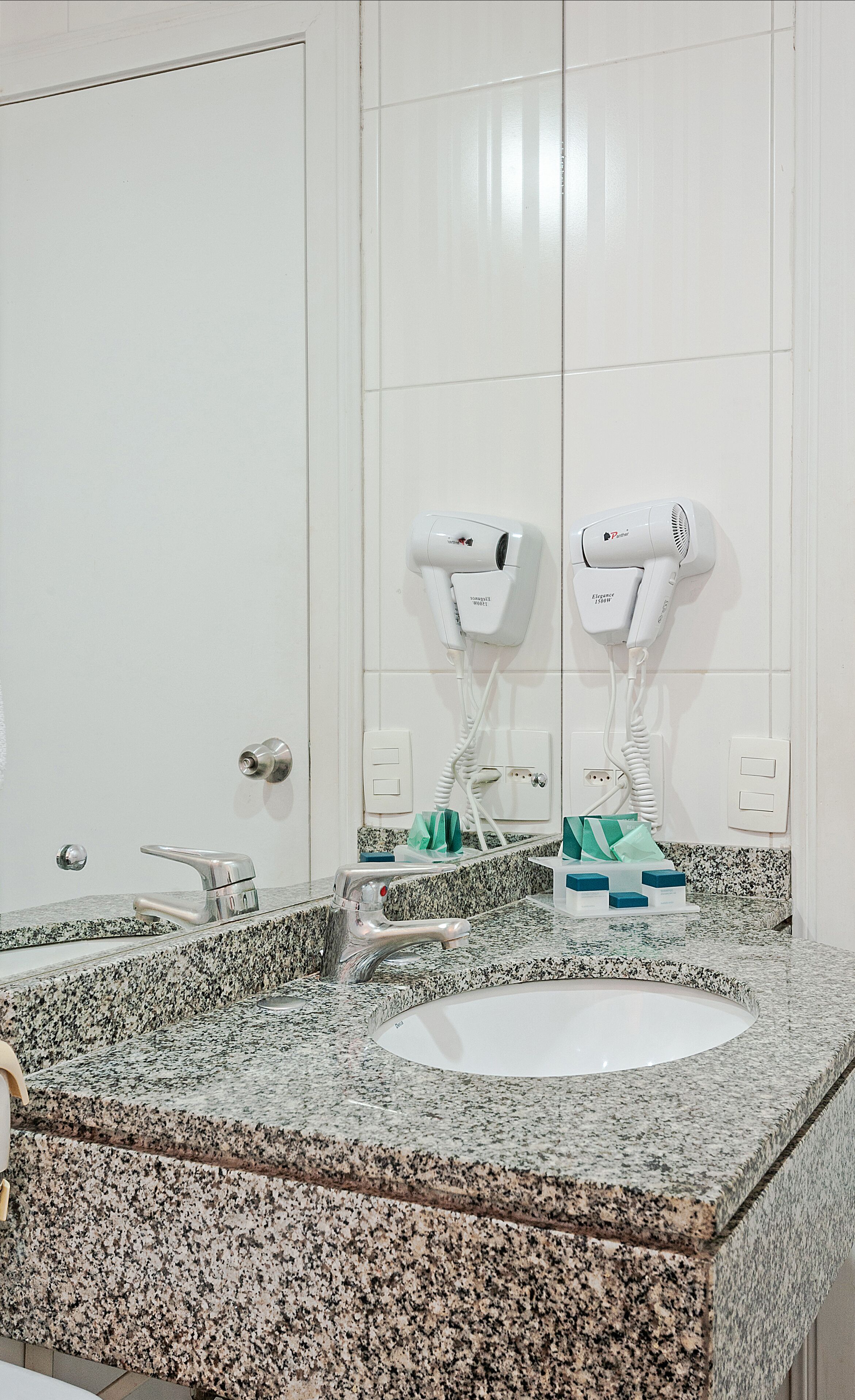 Une salle de bain avec deux lavabos, un miroir et deux sèche-cheveux fixés au mur.