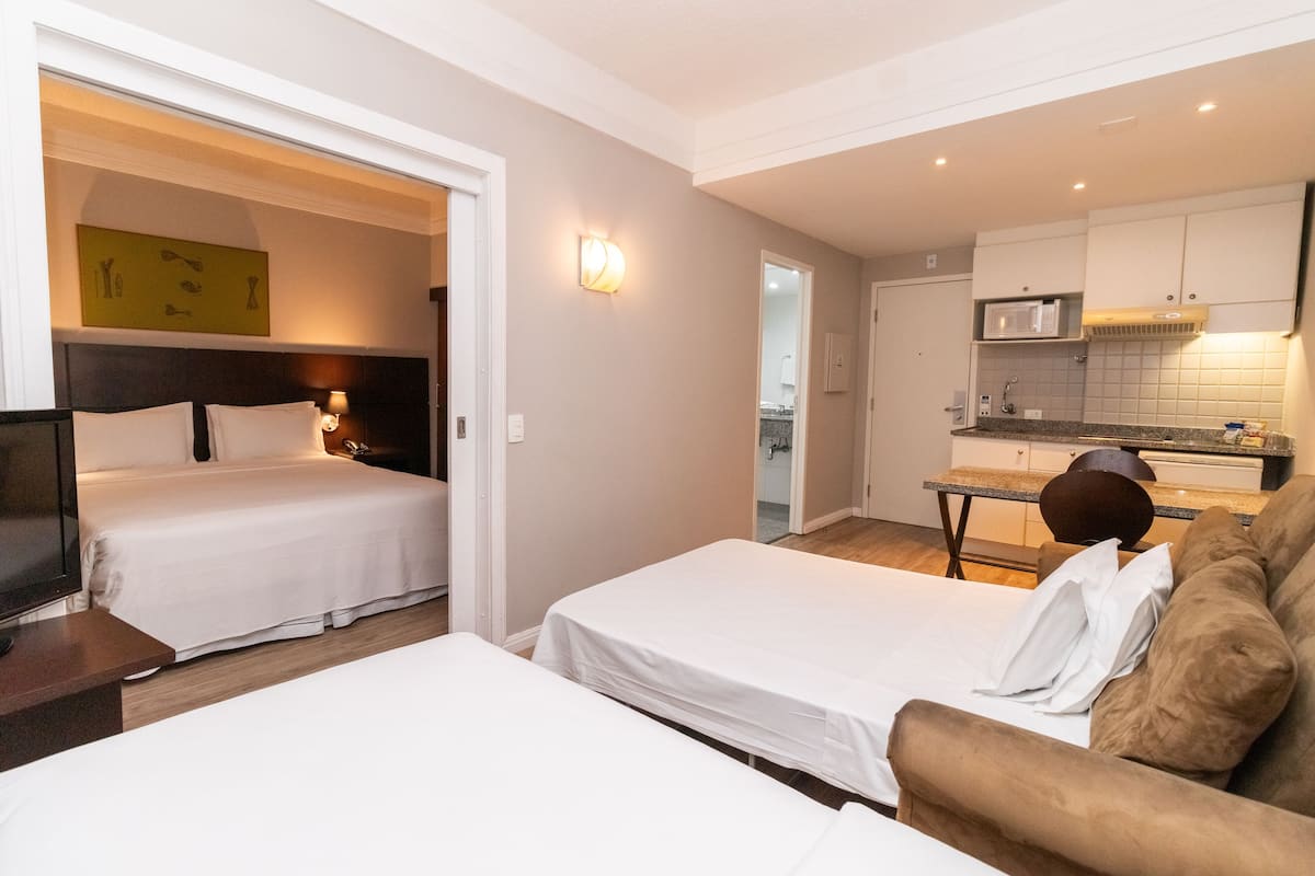 A hotel room with two beds, a sofa, a dining table, and a kitchenette.