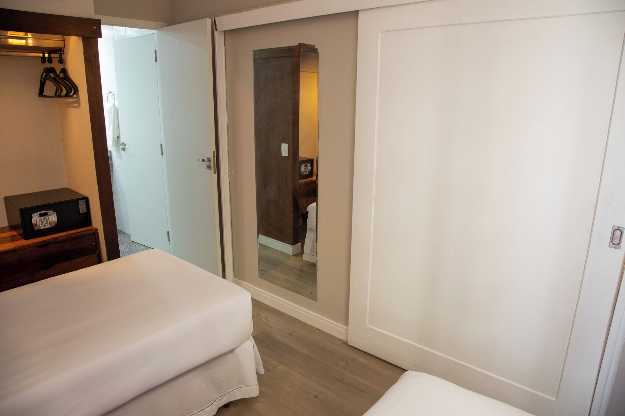 A hotel room with two beds, a wardrobe, a mirror, and a small table with a radio.