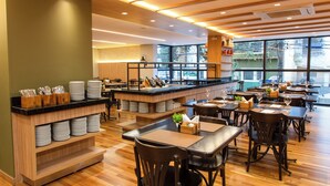 Restaurante moderno com piso de madeira, mesas pretas e uma ilha central com utensílios de cozinha.