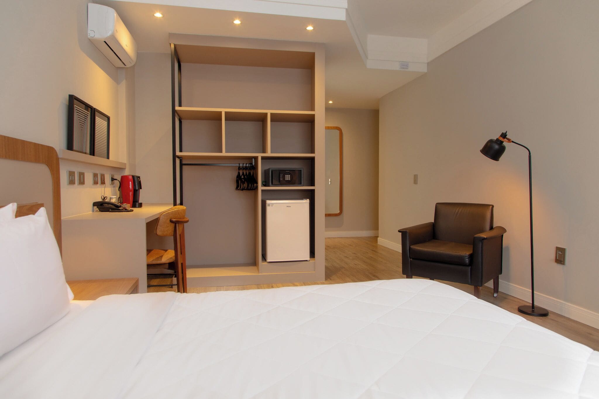 Habitación de hotel con cama, escritorio, silla, armario, microondas y lámpara.