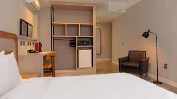 Habitación de hotel con cama, escritorio, silla, armario, microondas y lámpara.