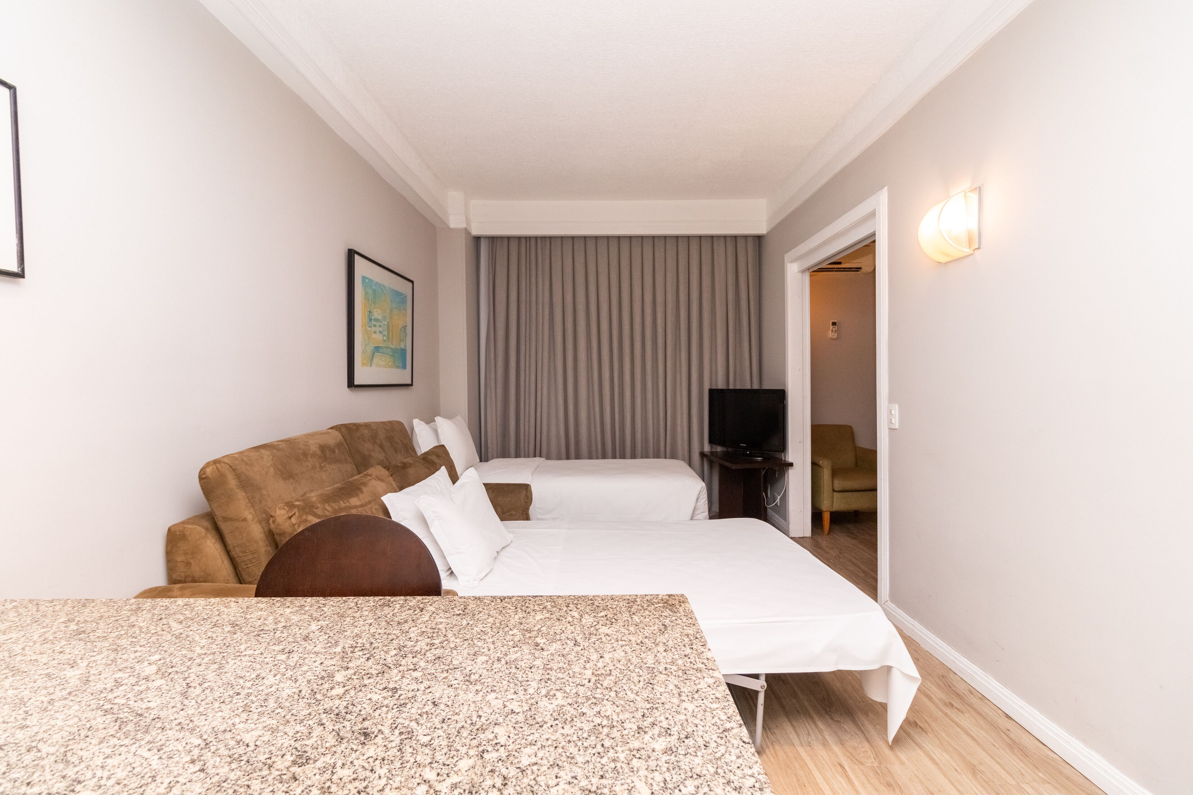 Quarto de hotel com cama, sofá, televisão e uma pequena mesa.