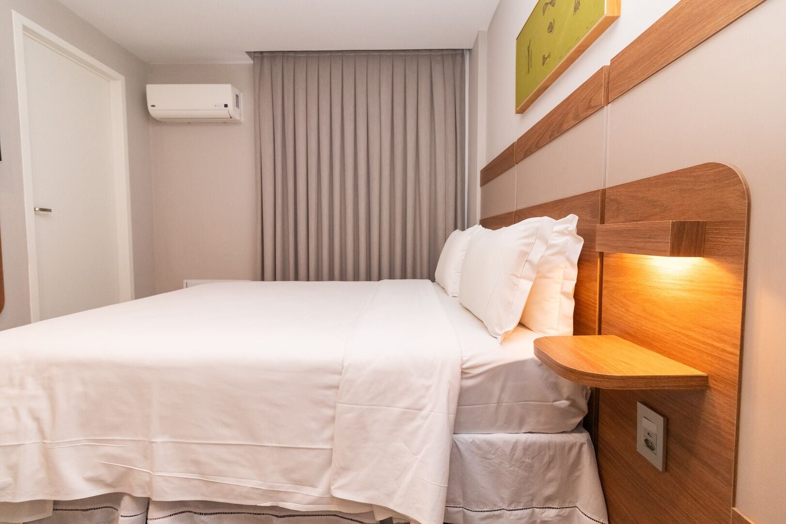 A neatly made bed with white bedding, a wooden headboard, and a bedside table with a lamp.