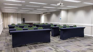 Sala de conferências com várias mesas e cadeiras, um projetor e uma máquina de café.