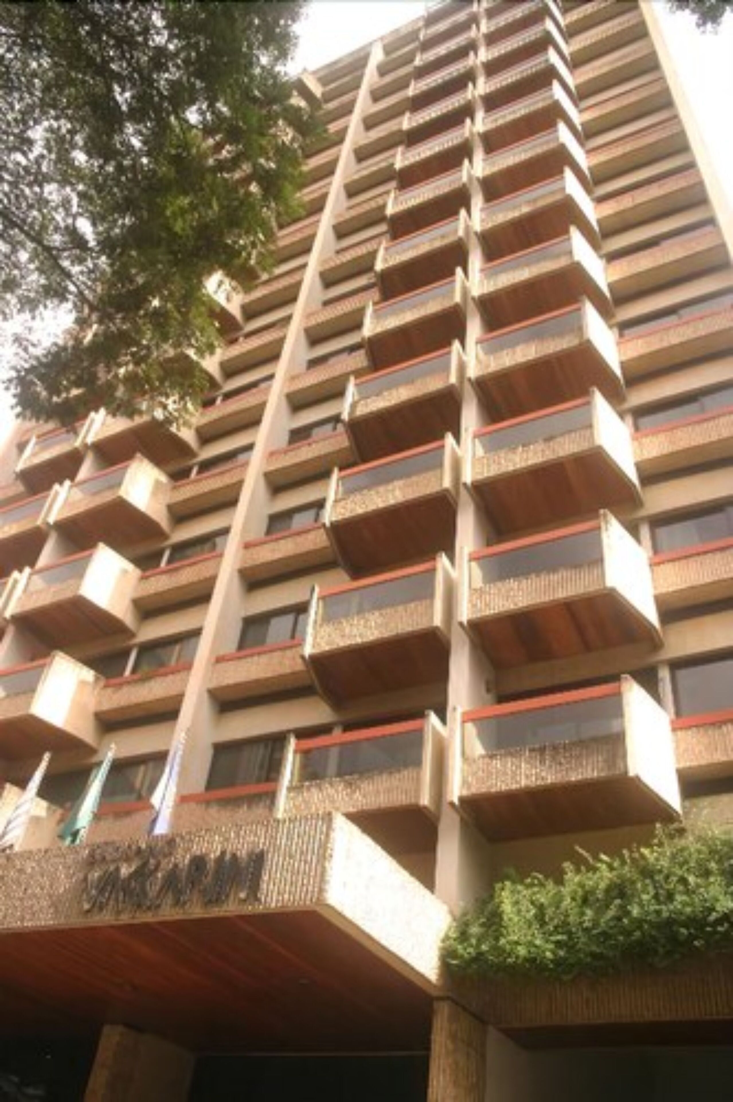 A high-rise building with multiple balconies, a sign indicating 'VANITY FAIR', and a small garden area at the base.