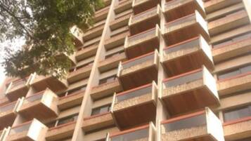 A high-rise building with multiple balconies, a sign indicating 'VANITY FAIR', and a small garden area at the base.