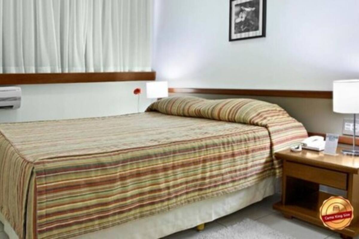 A hotel room with a bed, a bedside table with a lamp, a TV, and a window with curtains.
