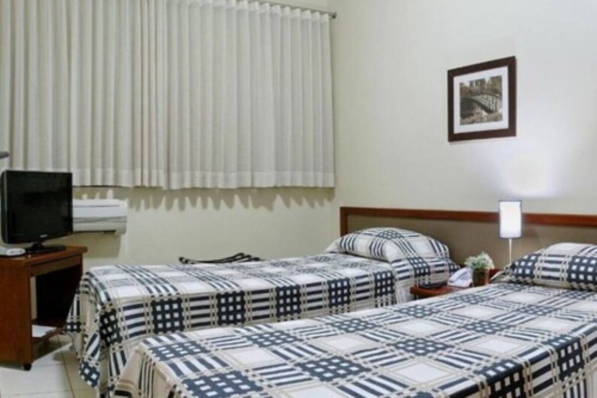 A hotel room with two beds, a television, and a framed picture on the wall.