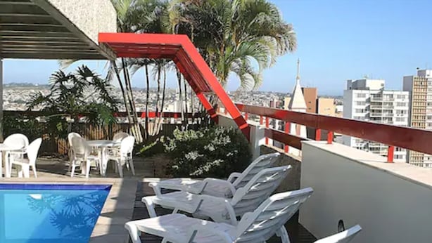 Un espace piscine sur le toit, avec des chaises longues blanches et une rambarde rouge.