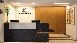 A reception desk with a black marble top and a wooden panel wall behind it. - Matiz Manhattan (São Paulo)