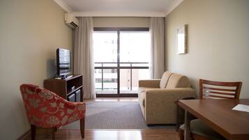 Una sala de estar con sofá, mesa de comedor, televisor y ventana con cortinas.